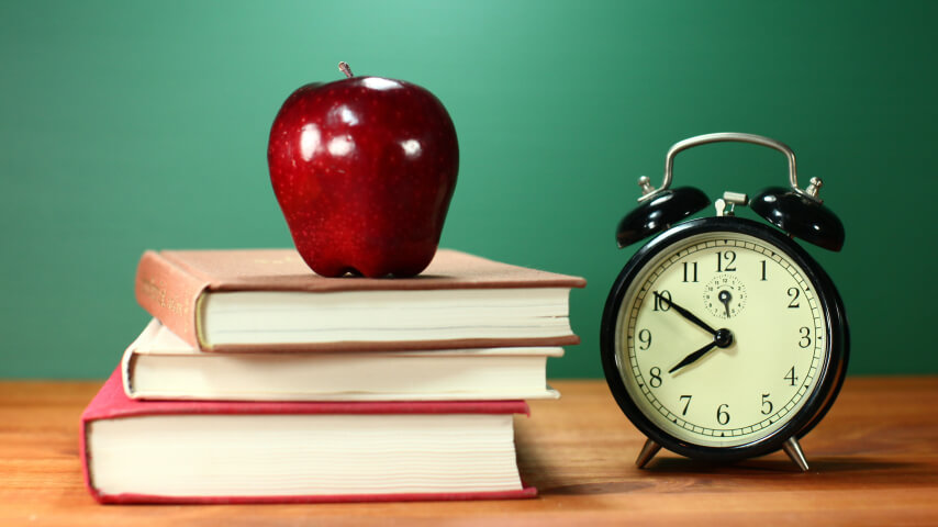 A back-to-school display with an alarm clock, stack of books, and a red apple
