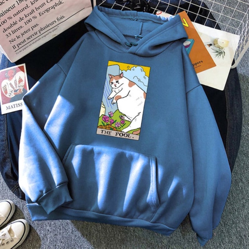 Blue hoodie with a design depicting a crying chunky meme cat on a tarot card captioned “The Fool.”