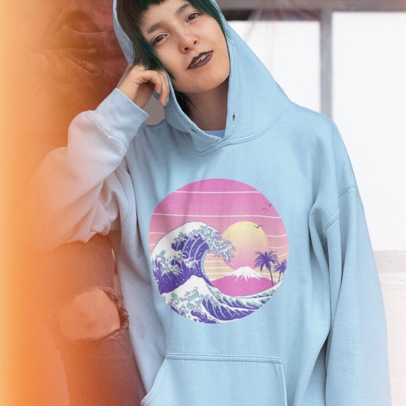 Woman wearing a light blue hoodie with a vaporwave design of beach waves in front of an island.