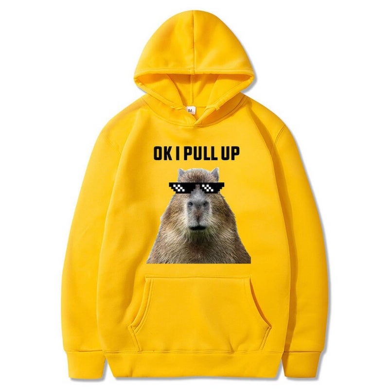 Yellow hoodie with an image of a capybara with pixel sunglasses and the text “OK I pull up” above it.