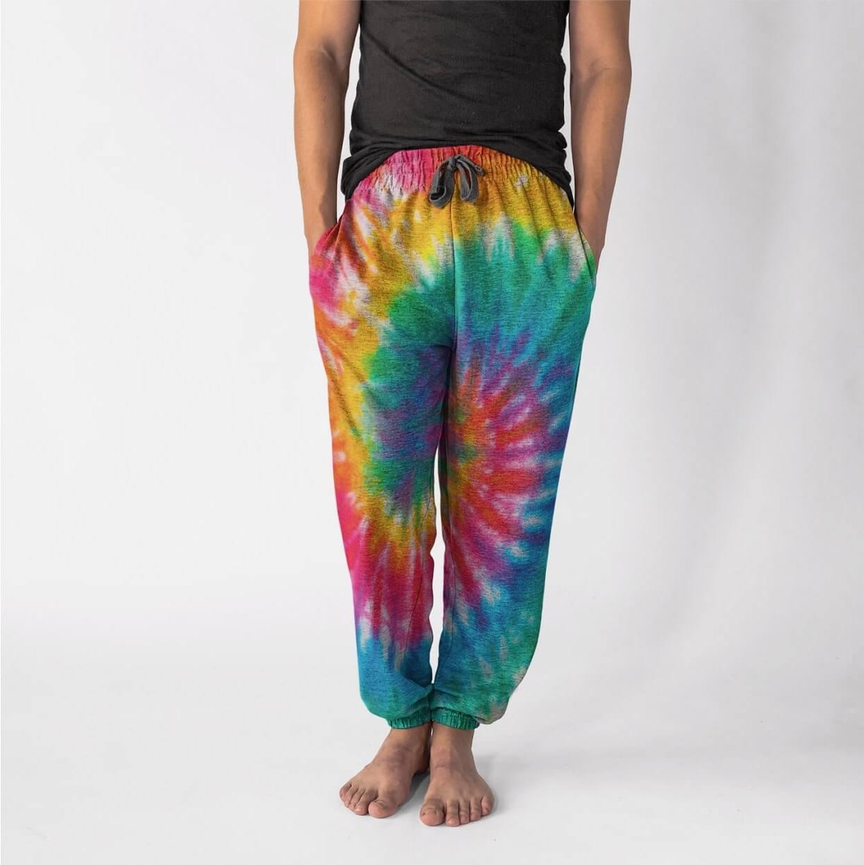 A barefoot man wearing a black t-shirt and colorful tie-dye jogger pants with a pattern resembling a rainbow