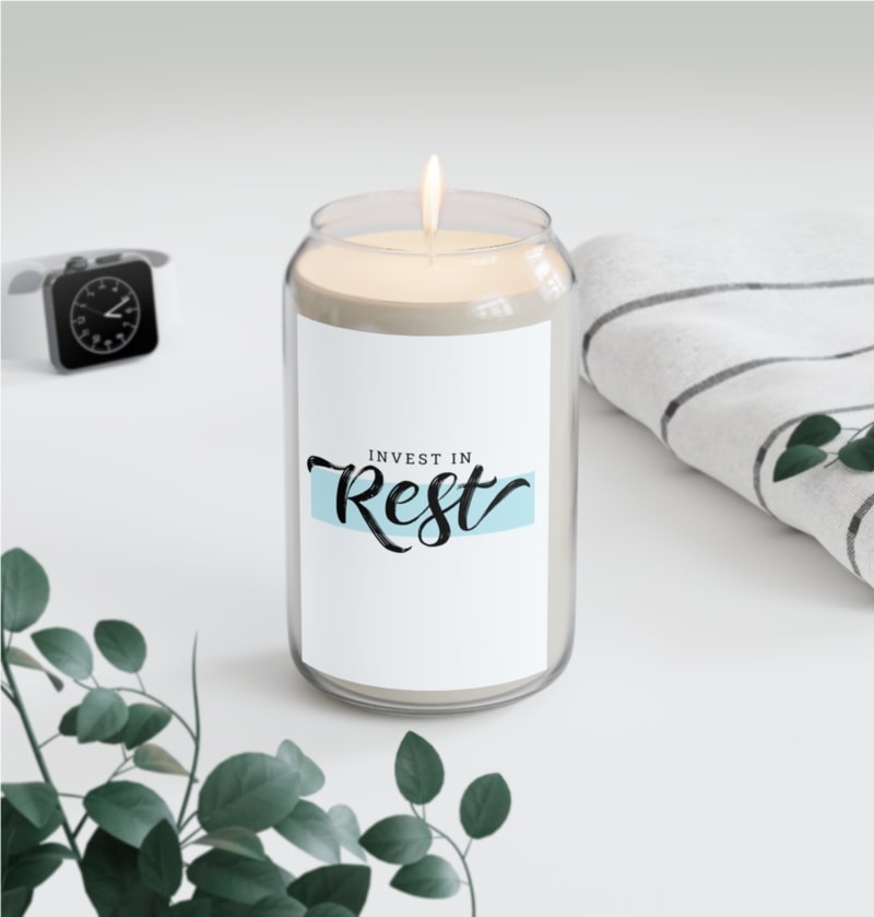 A cute home setup with a scented candle that has a custom design saying "Invest in rest"