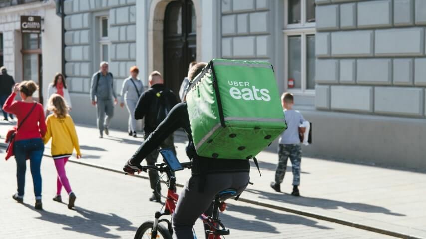 Uber Eats courier with a green backpack delivering food on a bicycle.