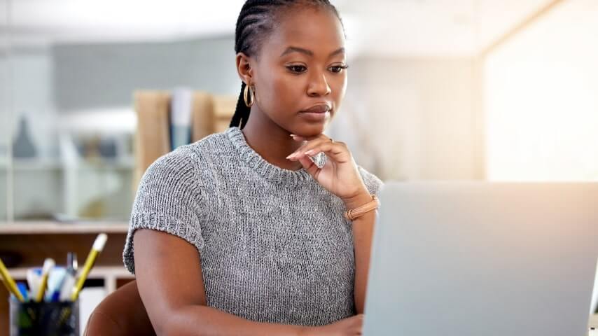 Woman researching lucrative affiliate marketing niches on her laptop with a thoughtful expression.