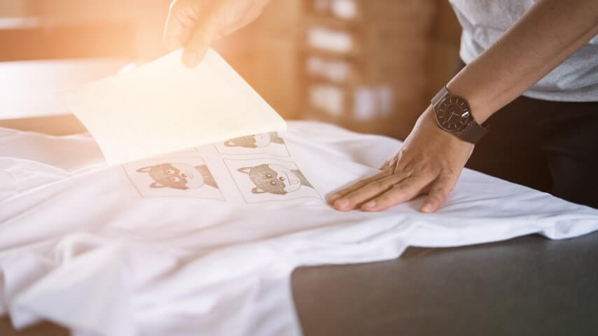 Person removing the transfer paper from a white t-shirt, revealing the design that is now printed on it.