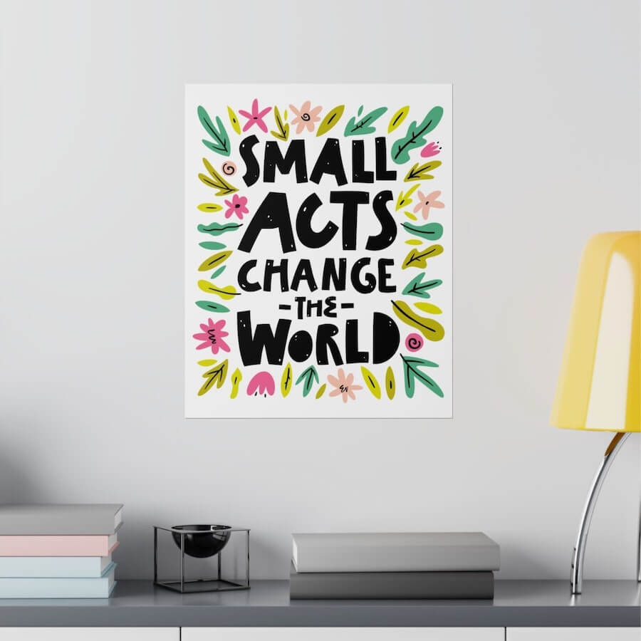 An image of a custom poster hanging on a wall with “Small Acts Change the World” writing on it with abstract illustrated floristics.
