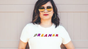 An image of a confident woman in sunglasses wearing a white t-shirt that says, Dreamer.