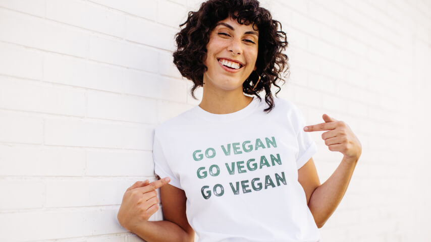 An image of a smiling woman pointing to her white t-shirt that says, Go Vegan.