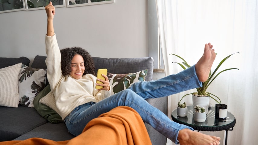 A young woman sitting on the couch, celebrating scoring a great Black Friday deal
