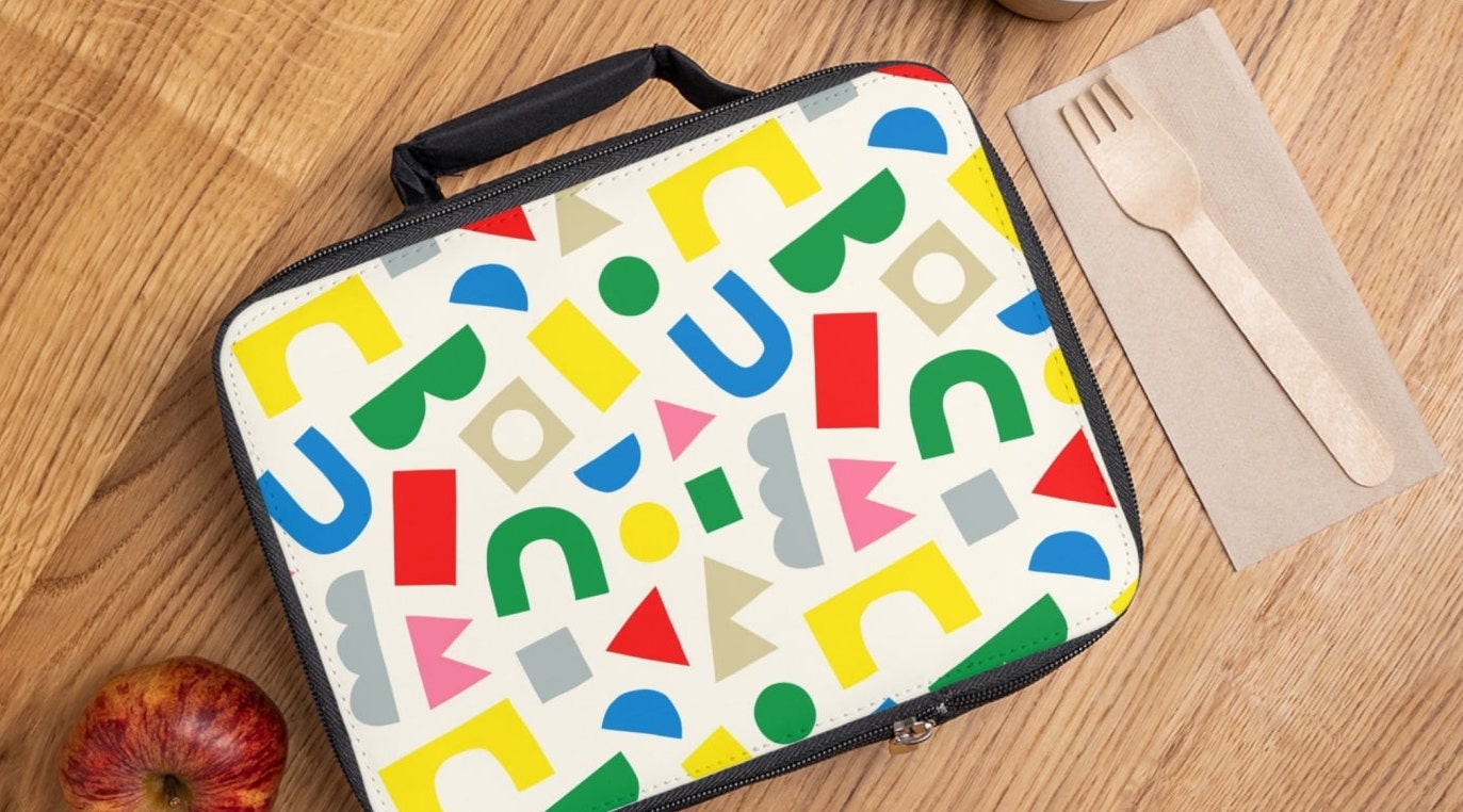 A personalized lunch bag with colorful abstract lettering, placed on a wooden table.