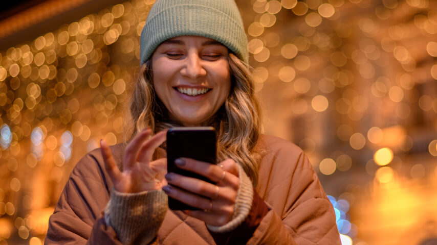 A happy holiday shopper scrolling through holiday promotions on her favorite sales channels.