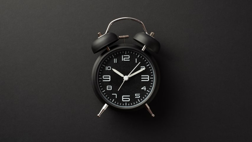 A black alarm clock displayed on a dark grey table reminding you to get ready for the Black Friday sales