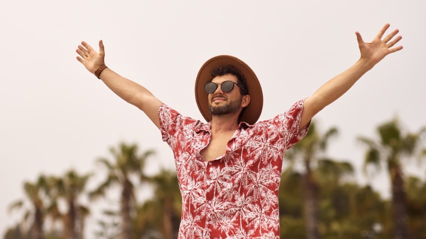 A man wearing a sublimated Hawaiian shirt with a pattern of red and white palm trees.