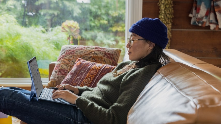 A woman sitting on a sofa sideways with her laptop on her lap.