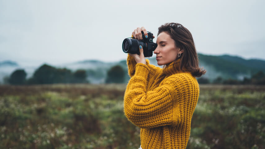 A woman standing in a field, taking photos with a professional camera.