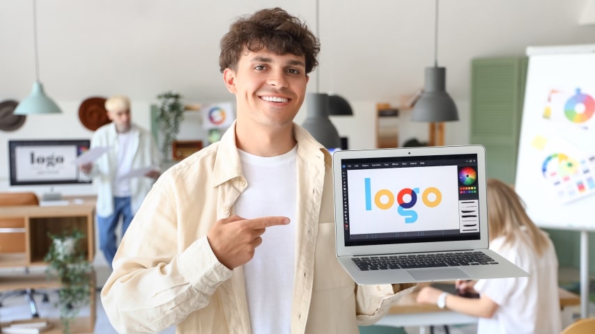 A man holding up his laptop to show a logo design file in Photoshop.