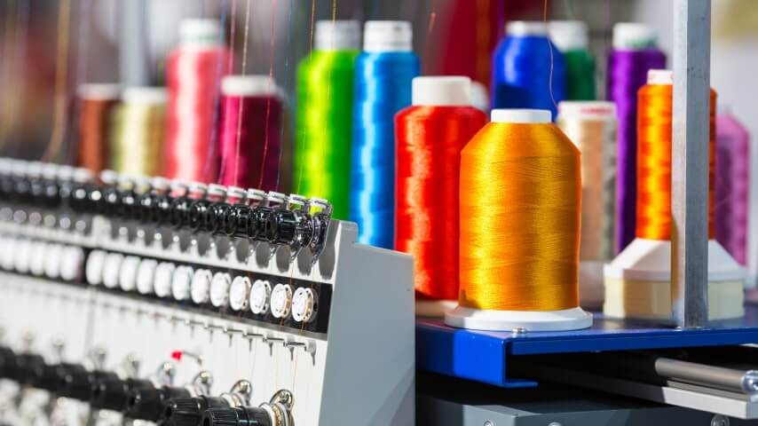 Various colorful thread spools on top of an embroidery machine.