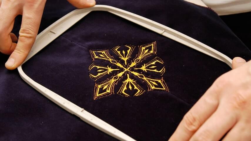 A person positioning a black piece of fabric for embroidery.