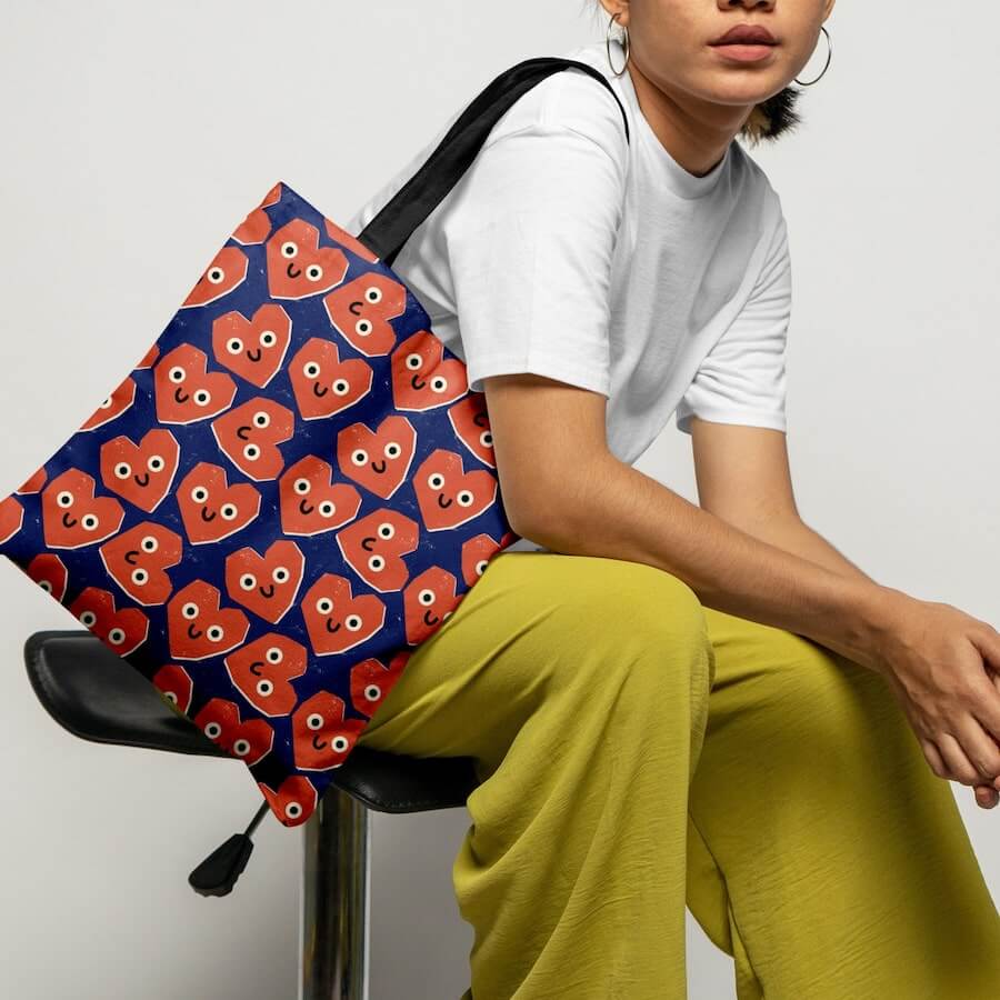 A woman with a dark blue tote bag with a pattern of smiling red hearts printed all over it.