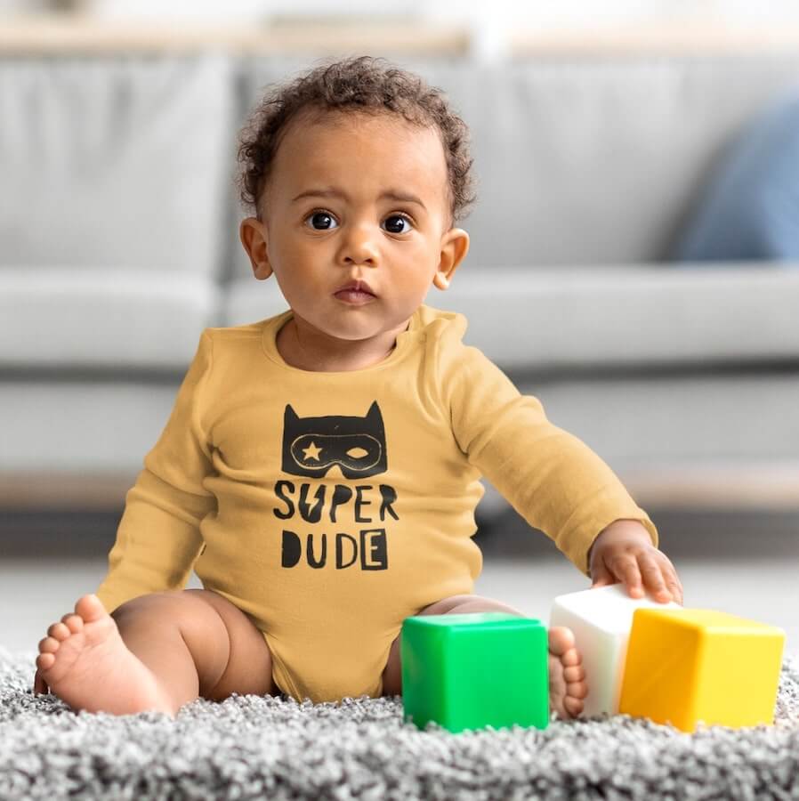 A child wearing an orange long-sleeve onesie with the text “Super Dude.”