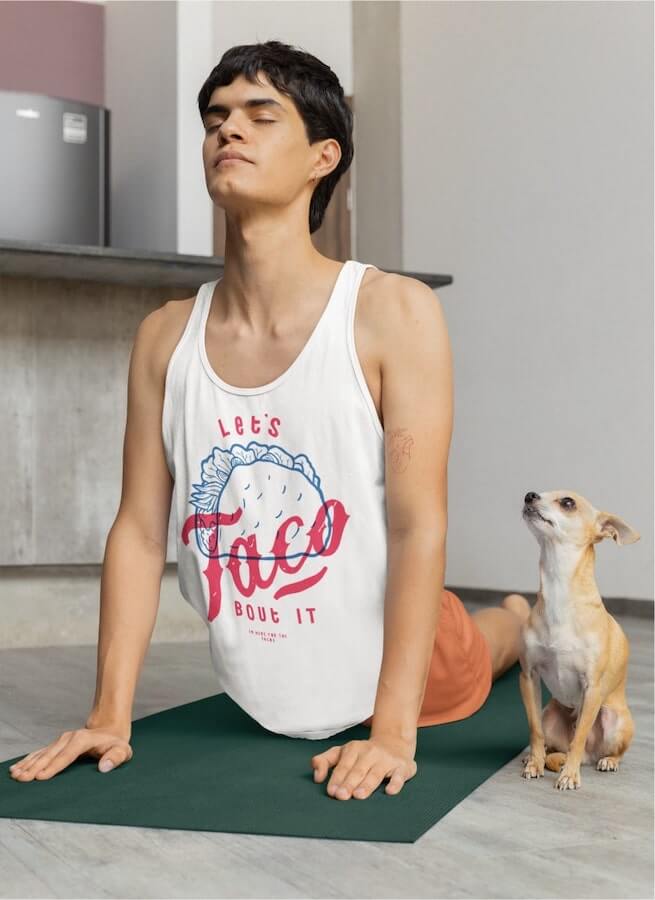 A man doing yoga and wearing a white tank top with a design of a taco and the text “Let's taco bout it.”