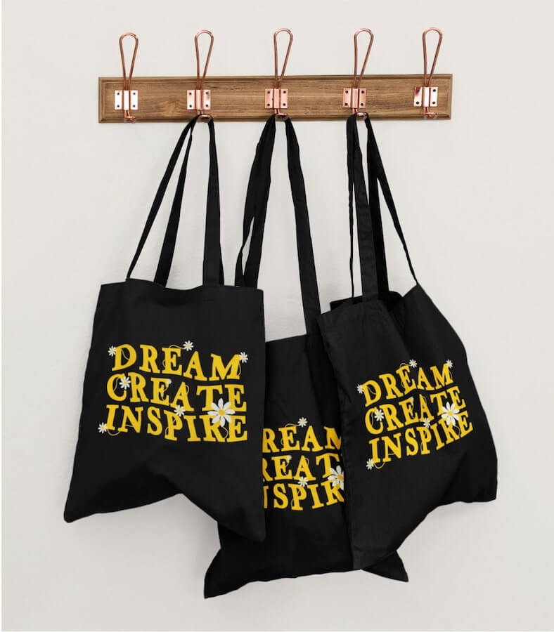 Black bulk tote bags with the text “Dream, create, inspire” printed on them in yellow letters.