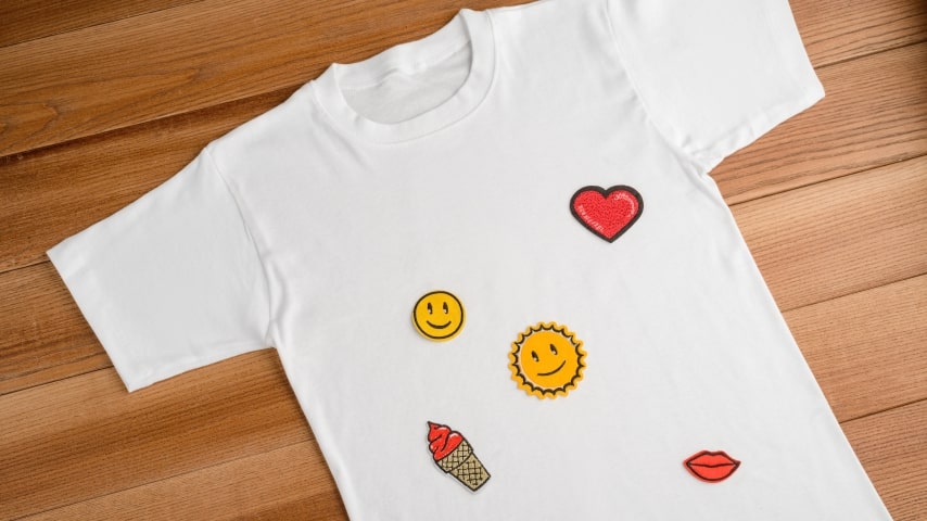 White t-shirt covered in small embroidered designs of smiley faces and hearts.