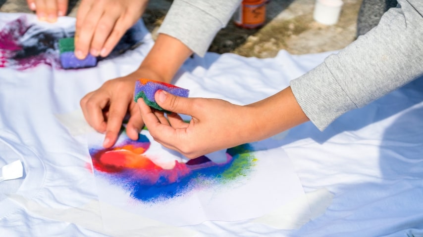 Person applying fabric paint on a white t-shirt.