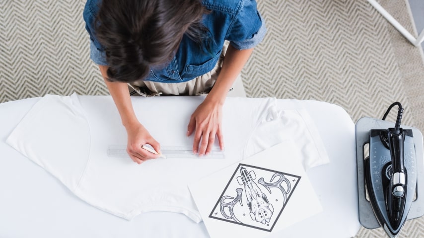 A man preparing a white t-shirt on which to iron a design with transfer paper.