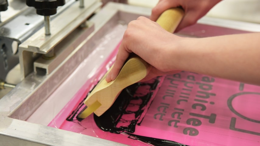 Person using a squeegee during the screen printing process.