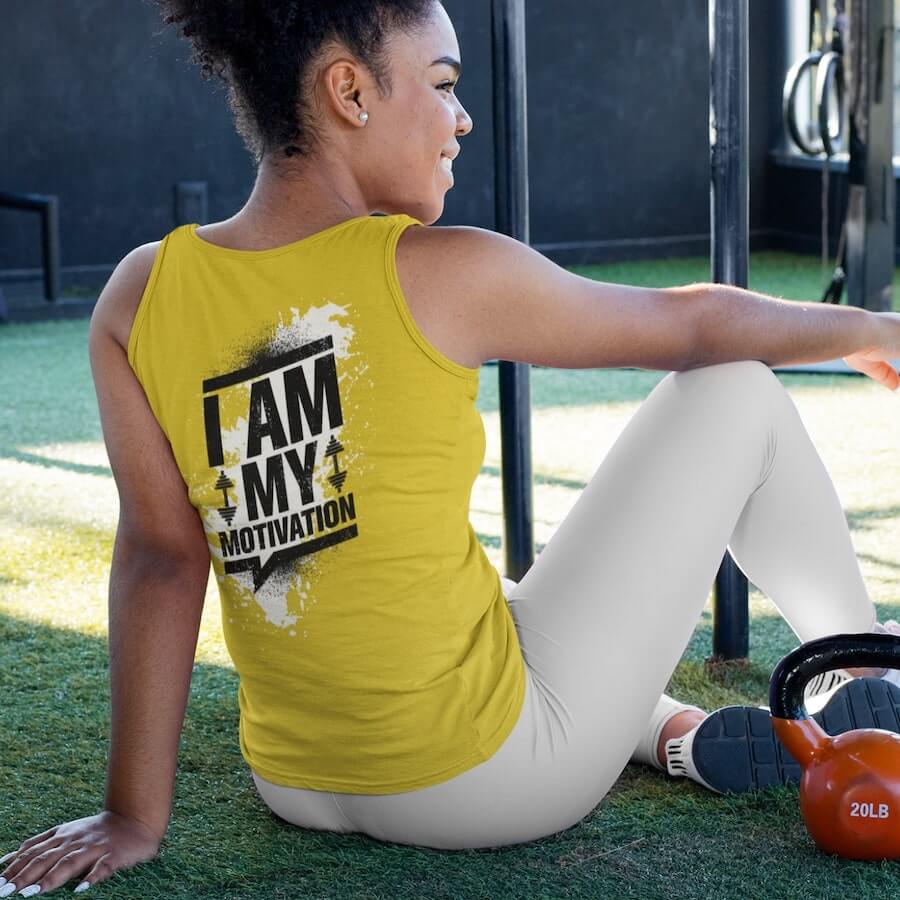 A woman wearing a yellow tank top with the text saying, “I am my motivation.”