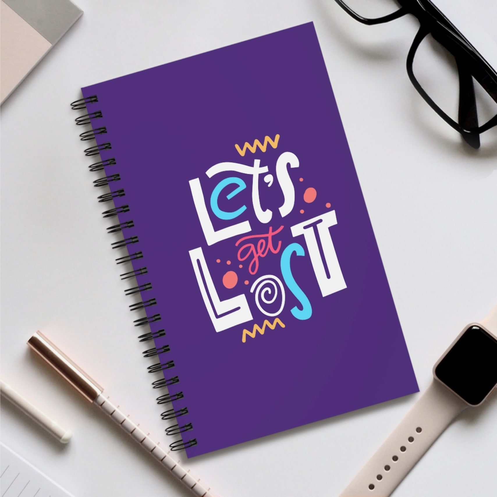 A purple spiral notebook with the text “Let’s Get Lost” printed on the front cover in colorful letters.