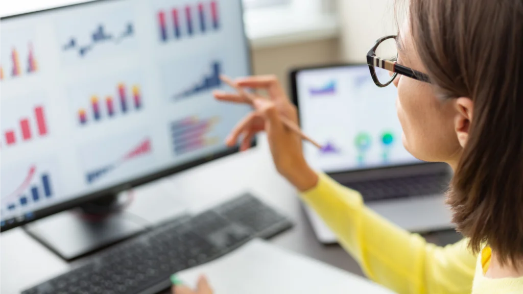 A woman analyzes graphs displayed on a computer screen, focusing intently on the data presented.