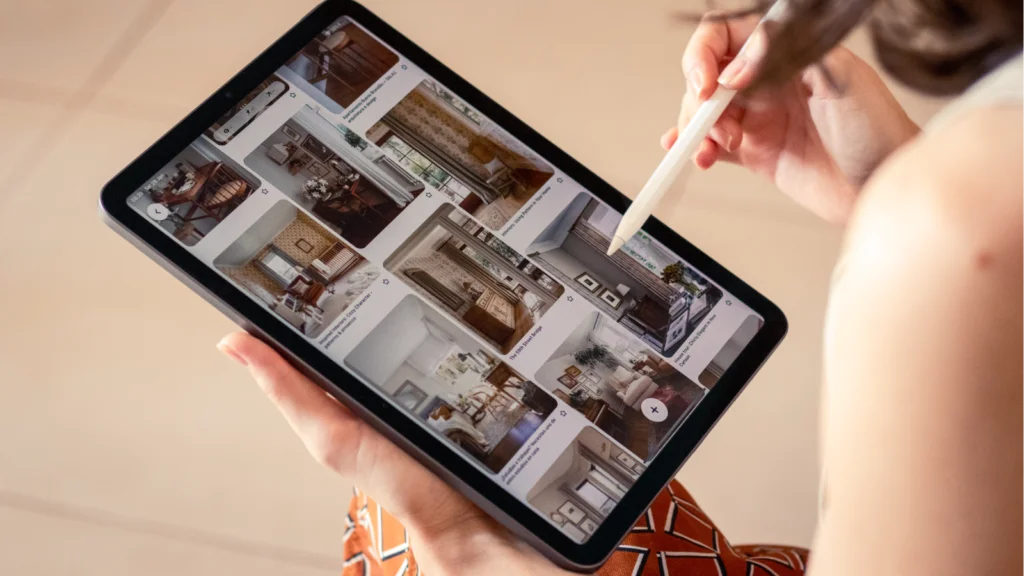 A woman holds a tablet displaying a photo of a house, smiling as she looks at the screen.