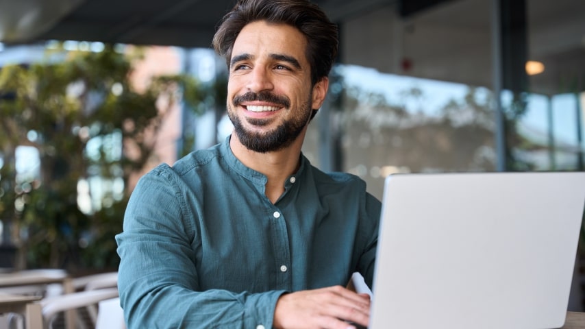 A smiling man with a laptop, learning how to sell on Walmart with Shopify.