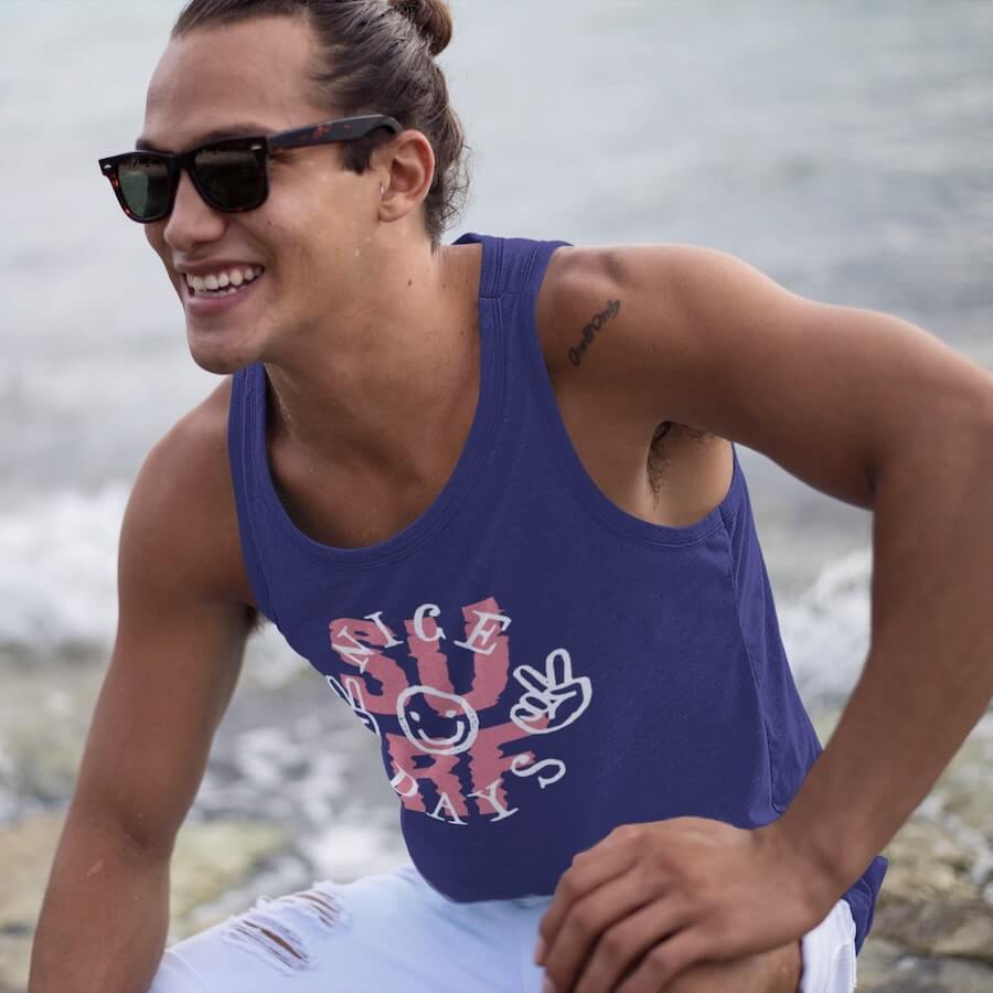 A man wearing a purple tank top with the text “Surf. Nice Days” and a design of a smiley face showing “peace” signs.