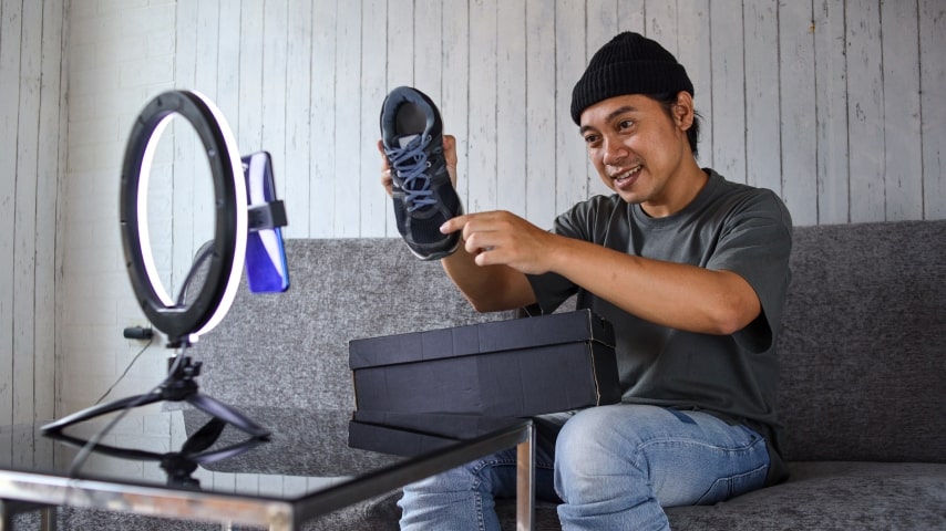 A young man making a video of himself reviewing shoes with his phone and a ring light.