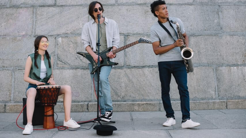 A band performing on the sidewalk and gathering donations into a hat.