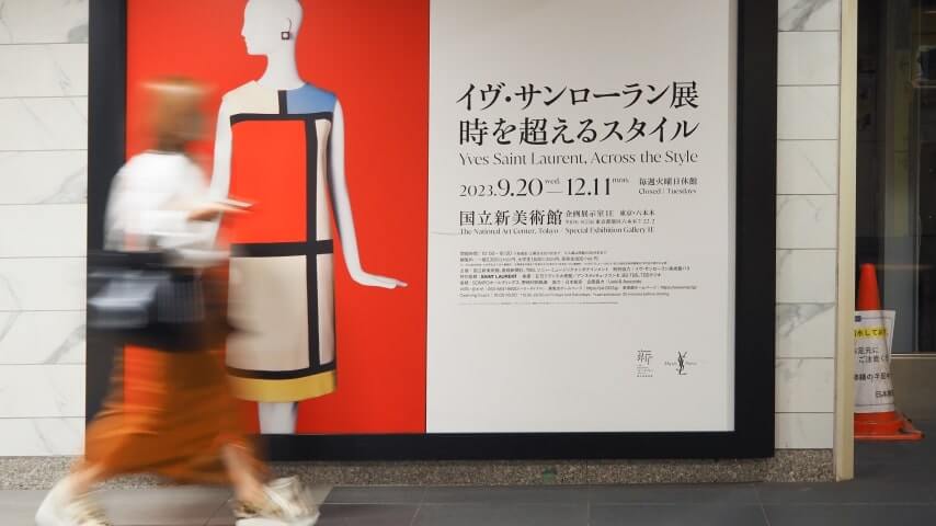 A woman walking past a large fashion poster ad on the street.