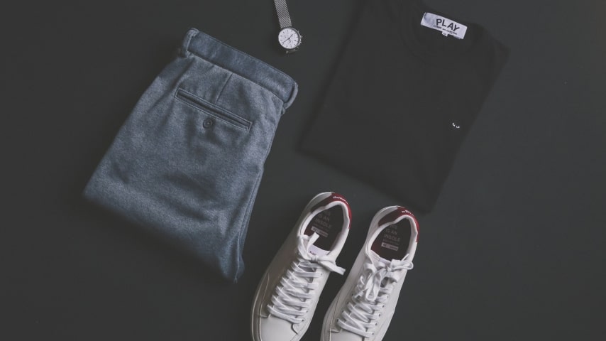 Black shirt, silver watch, grey pants and white shoes on black surface.