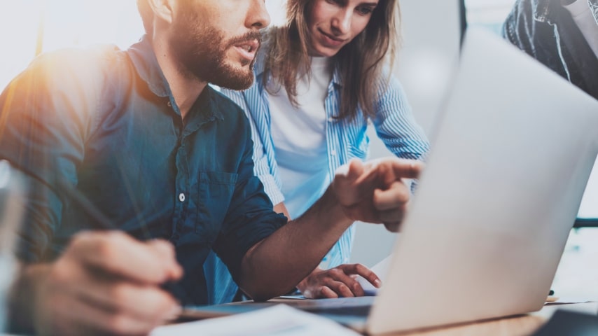 A man and a woman looking at a laptop screen and analyzing information.