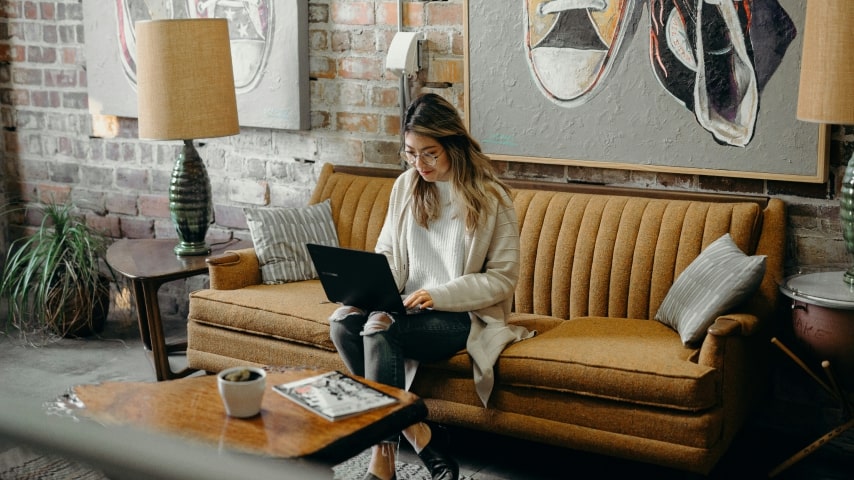 Woman sitting on a couch and holding a laptop.
