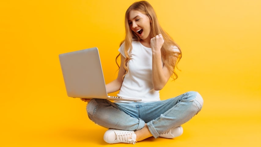 An image of a woman cheering while holding a laptop, all on a yellow background.