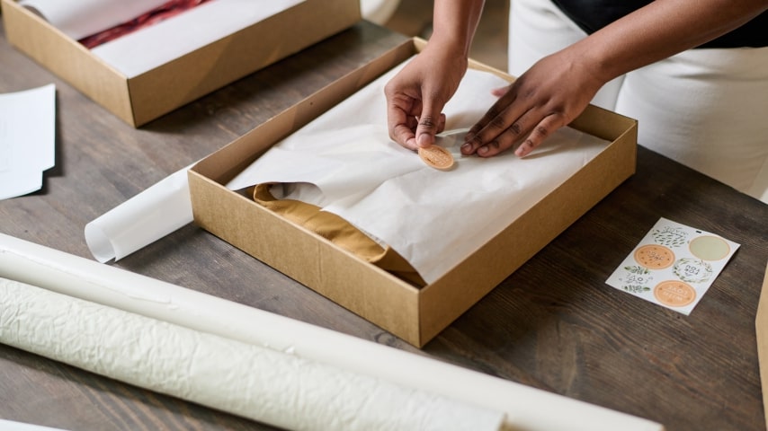A person placing a sticker on wrapping paper to seal the package for their Etsy order.