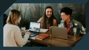 Header image of three people sitting at the table with their laptops on and laughing.