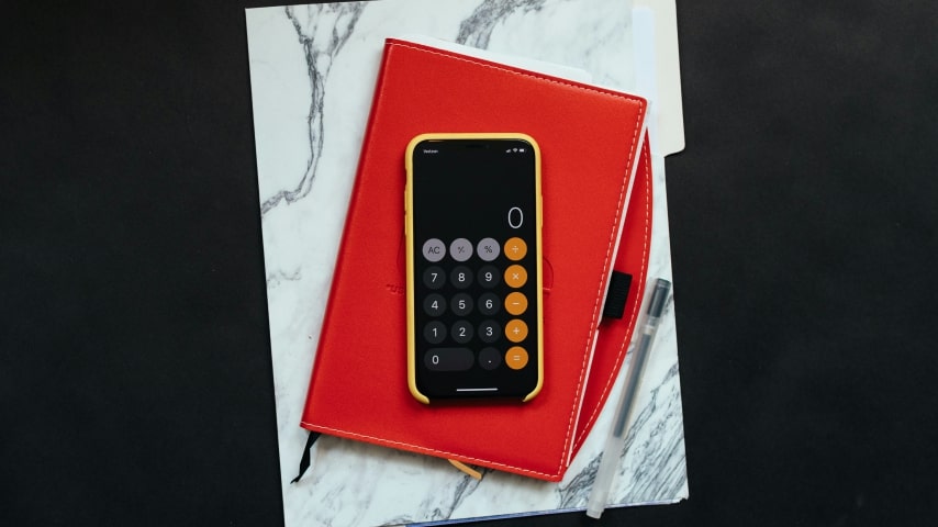 A phone with the calculator app open placed on a red notebook.