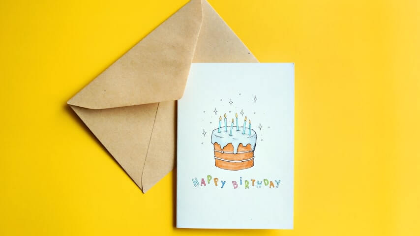 A greeting card with a design of a cake and the text saying, “Happy Birthday” placed next to an envelope.