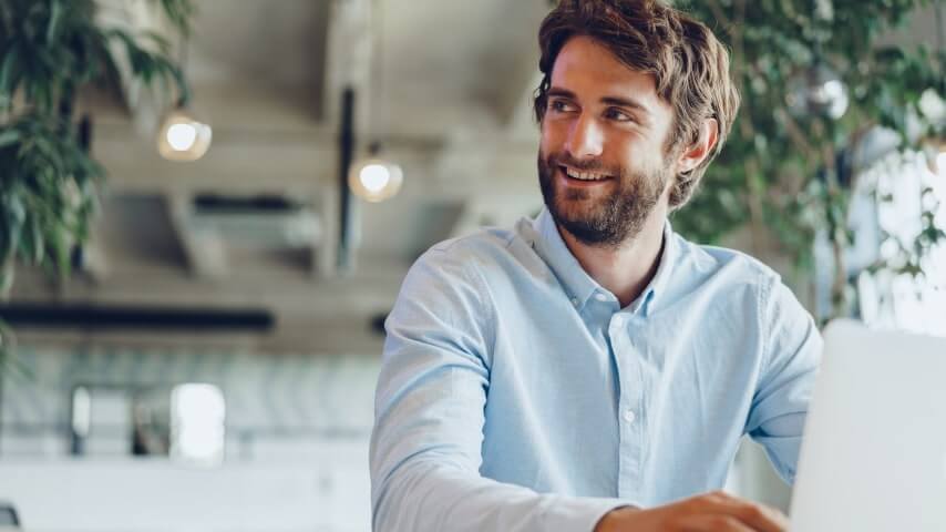 A man working on his laptop while looking thoughtfully into the distance.