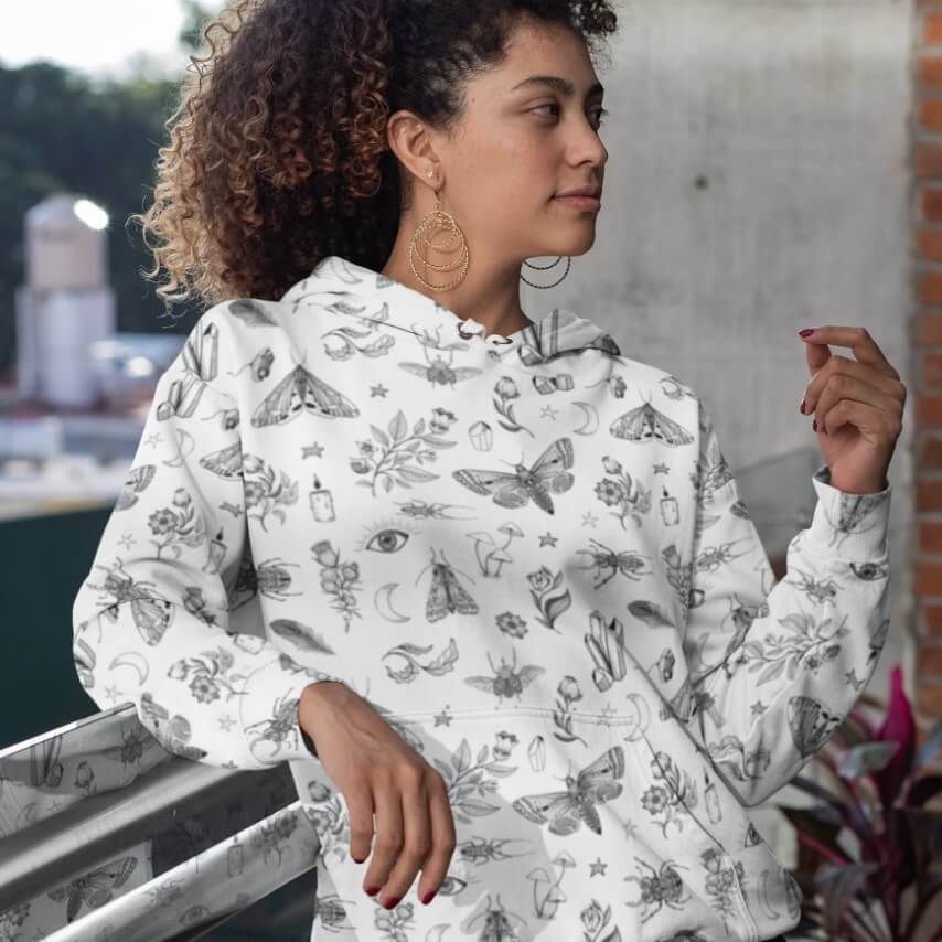 A woman wearing a white hoodie with a creative bug and flower pattern design.