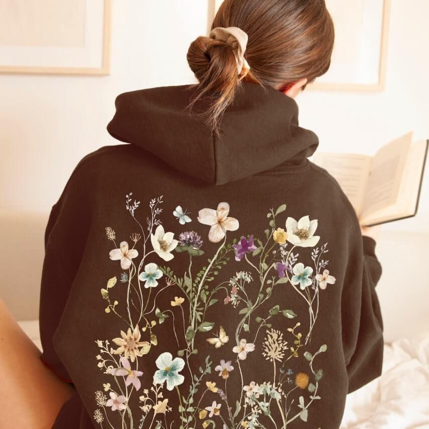 A woman wearing a black hoodie with a floral design on the back.